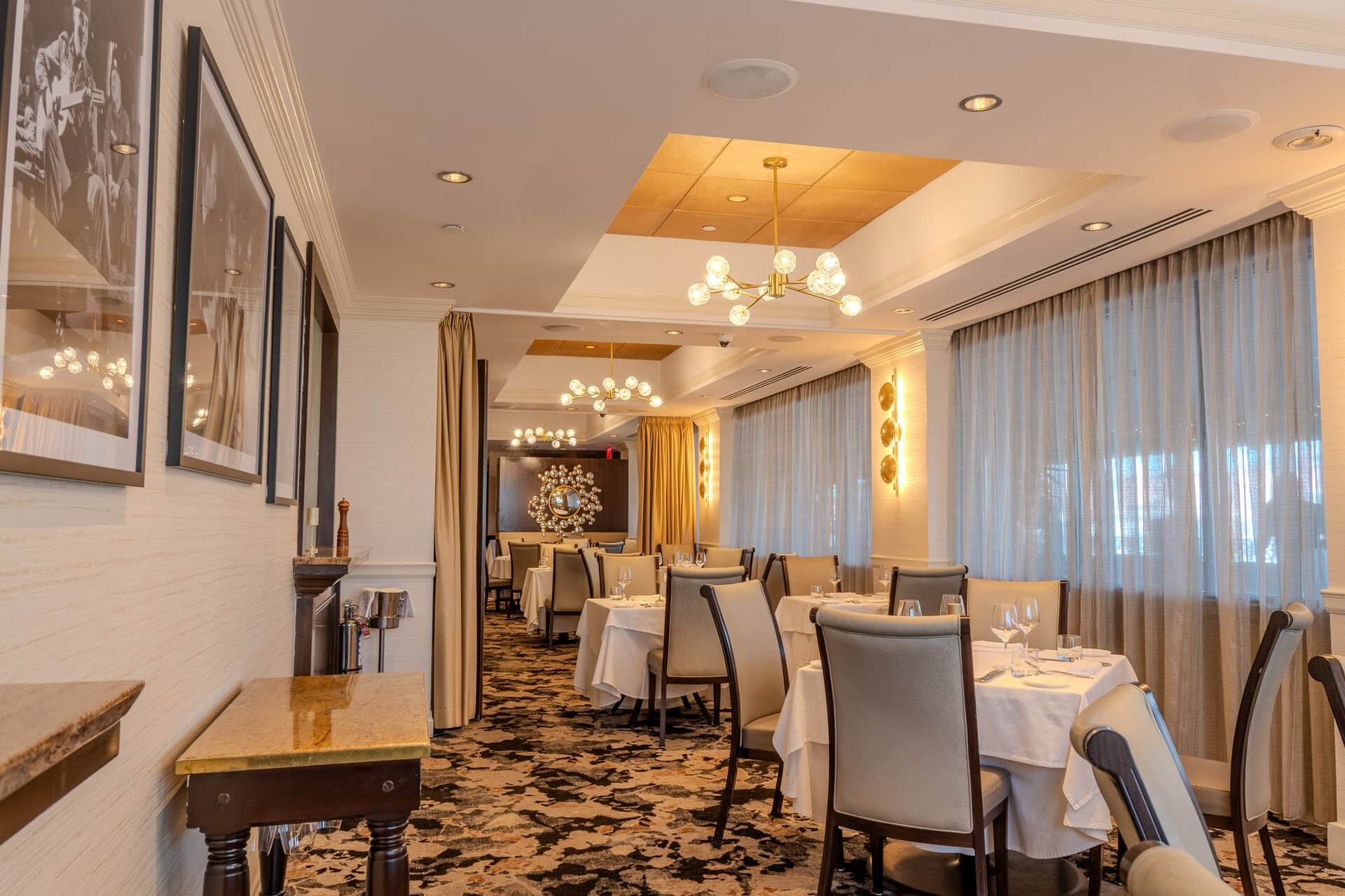 Dining room tables with white tablecloths beside sheer-curtained windows