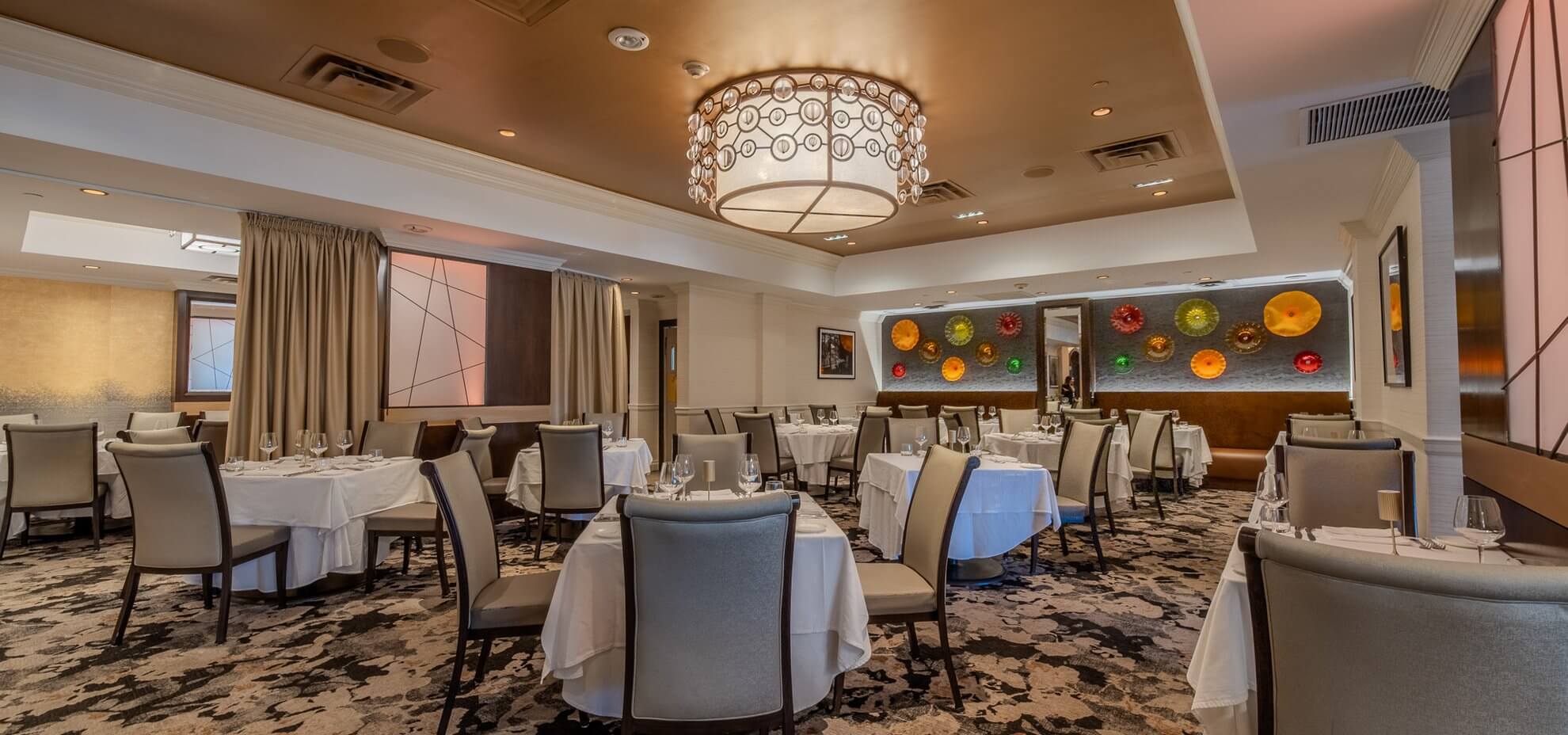 The dining room with white-clothed tables under a crystal chandelier and a wall of colorful glass plates