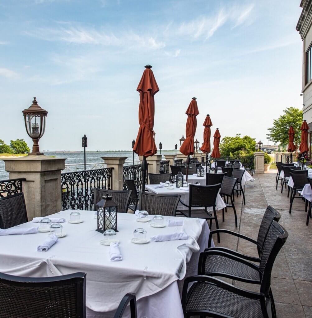 Waterfront Veranda tables with white cloths and red umbrellas beside Jamaica Bay