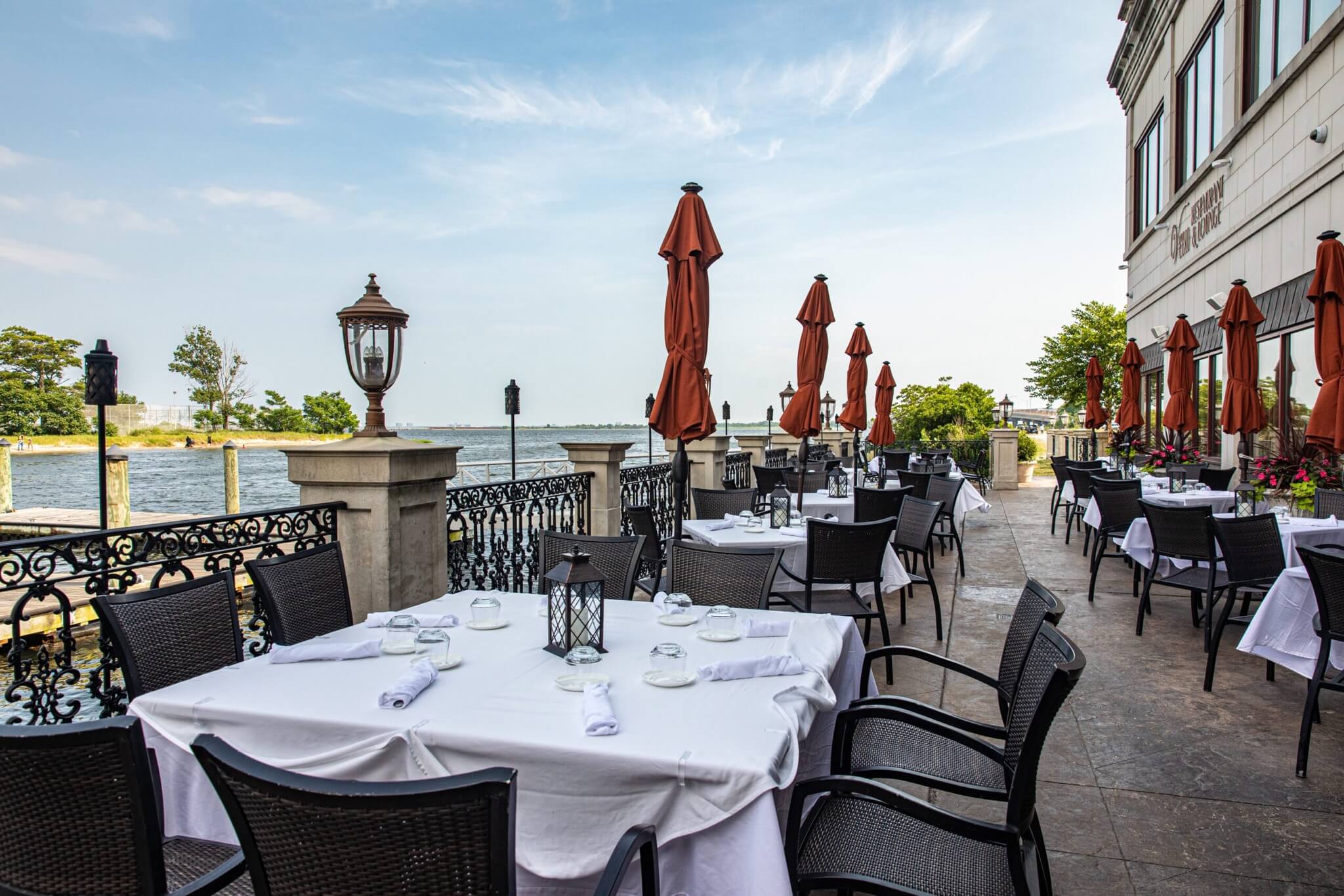 Waterfront Veranda tables with white cloths and red umbrellas beside Jamaica Bay